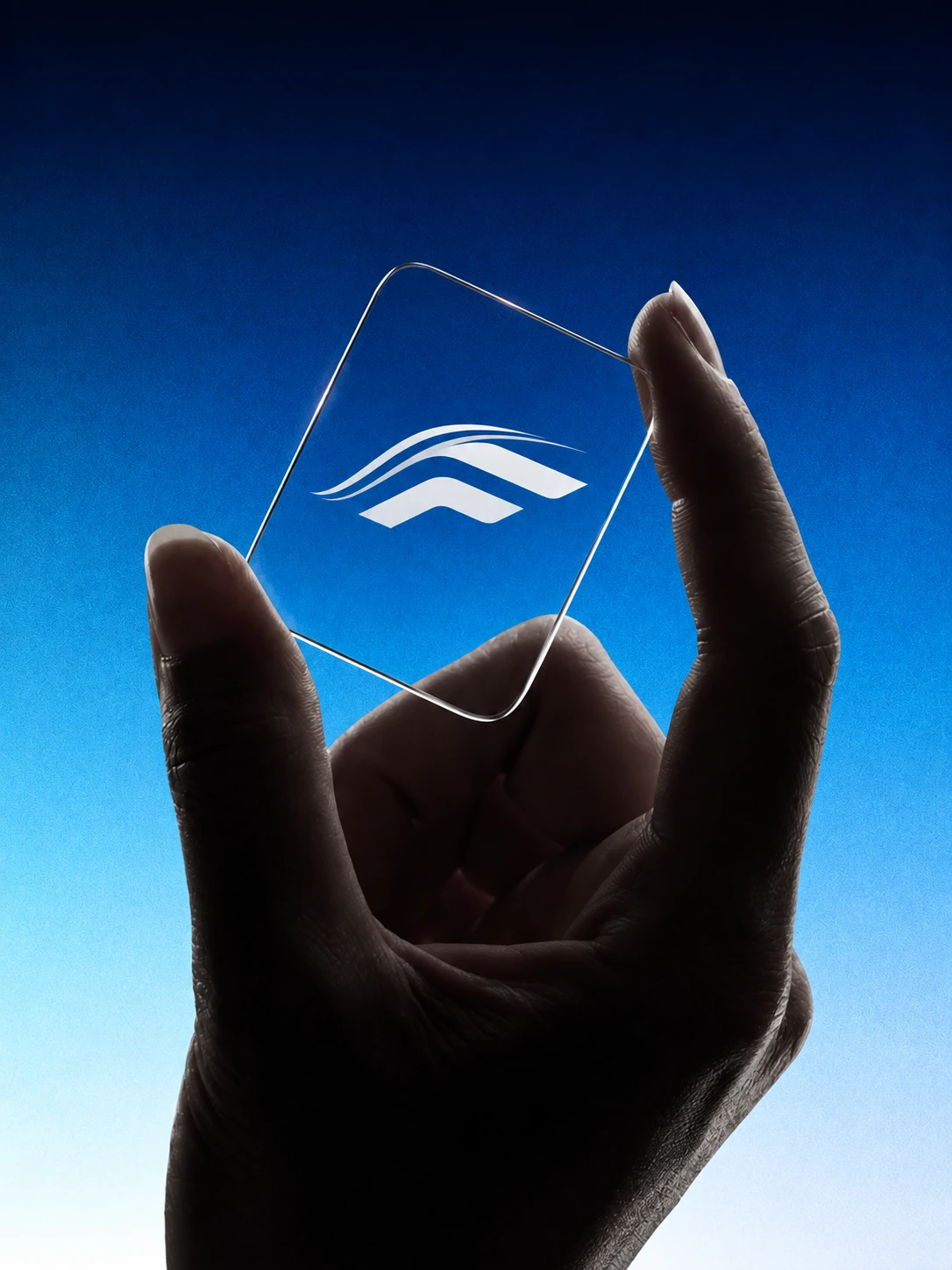 A hand holds a transparent glass plate with the Varra mark in front of blue light.